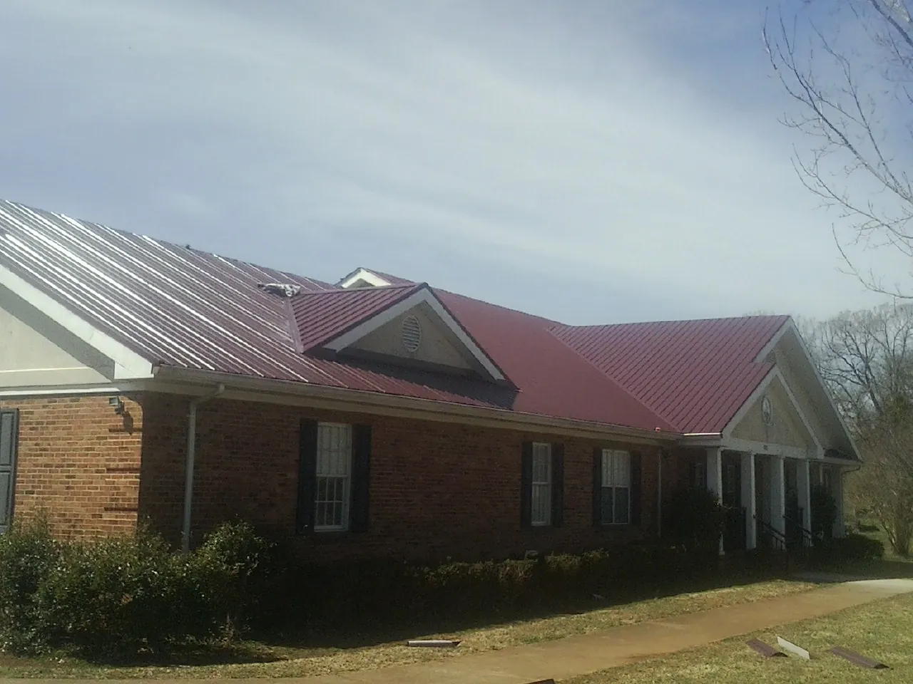 Red metal roof with gabled entries on a long brick building, from a Hail Damage Roof Repair job in Elwood