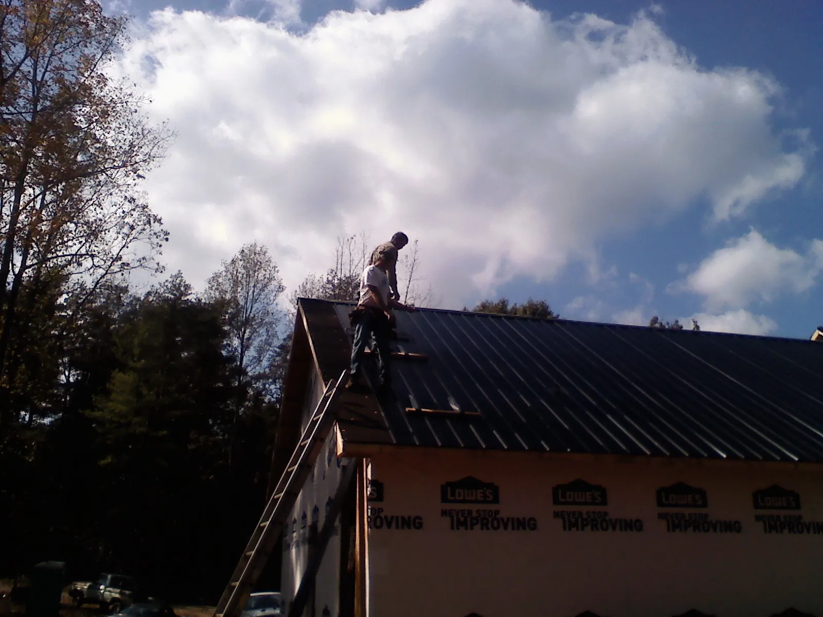 Roofer fastening dark metal panels high against a cloudy sky, from a Roof Inspection job in Elwood