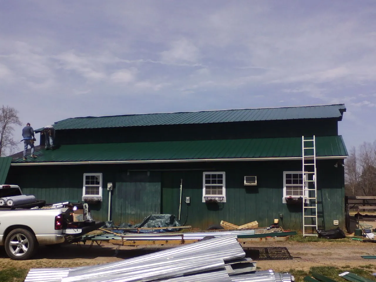 Crew installing green metal roofing on a large green barn in Elwood